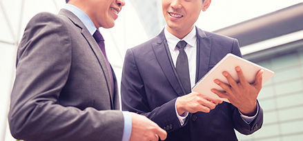 two man in suits discussing with a tablet in hand