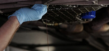 gloved hand working oil filter at the bottom of a vehicle