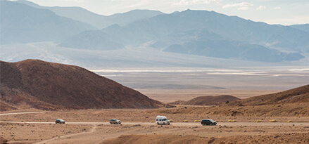 Line of cars driving on a straight road past hilly terrain