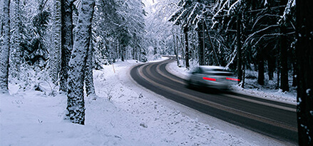 Fast car driving on a road surrounded by snow and trees
