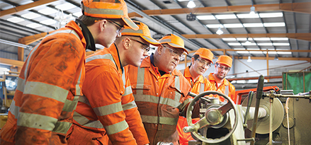  group of engineers in orange looking at machine
