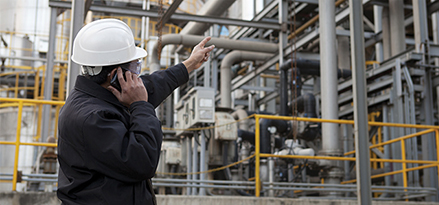 engineer talking on phone and pointing at refinery