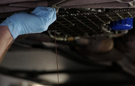 Gloved hand working oil filter at the bottom of a vehicle